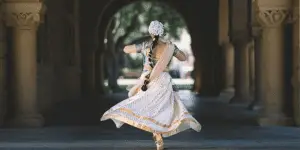 An image of a woman in traditional Indian dance costume, all white with gold trimming, twirling in an archway.