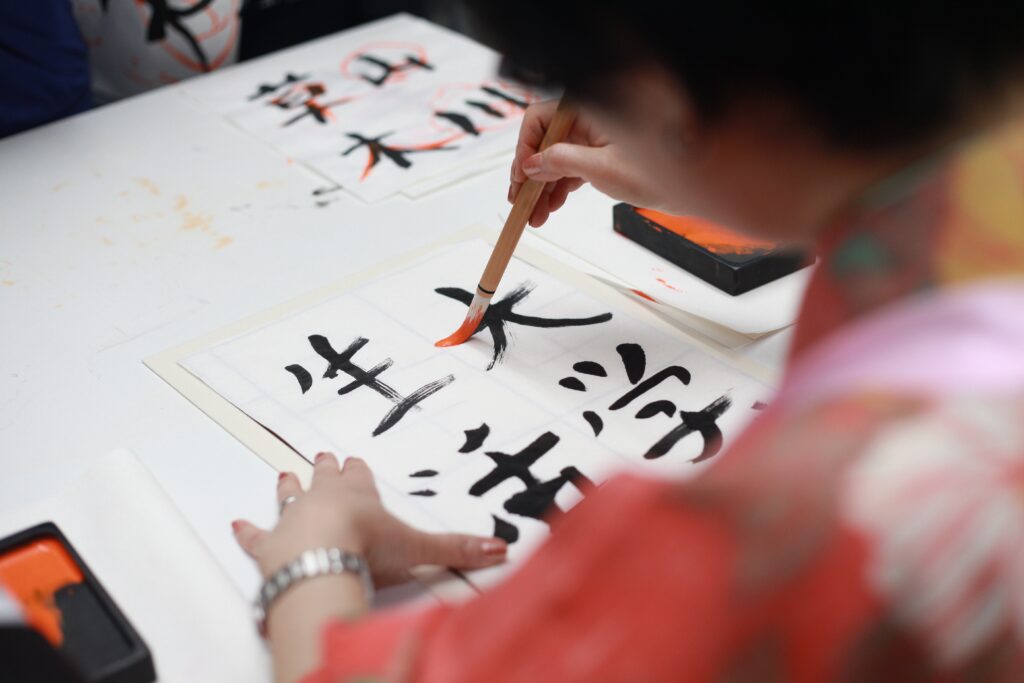 A woman bends over a piece of paper to write kanji with a calligraphic brush. It's a bit advanced for those wishing to learn Japanese, but it could be good practice!