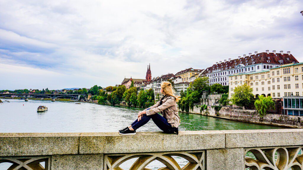 A woman in a grey jacket sitting on the edge of a bridge in german. German coffee breaks featured image.