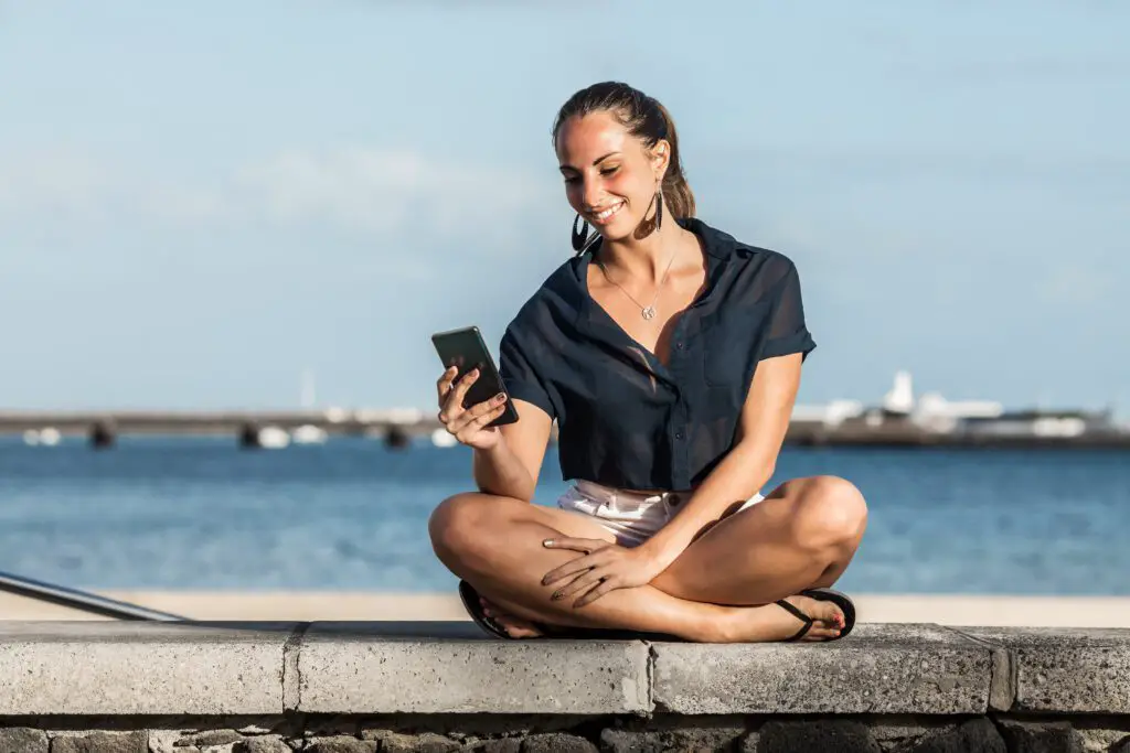 Smiling woman using smartphone on embankment in summer. Featured image for Ling App Review article.