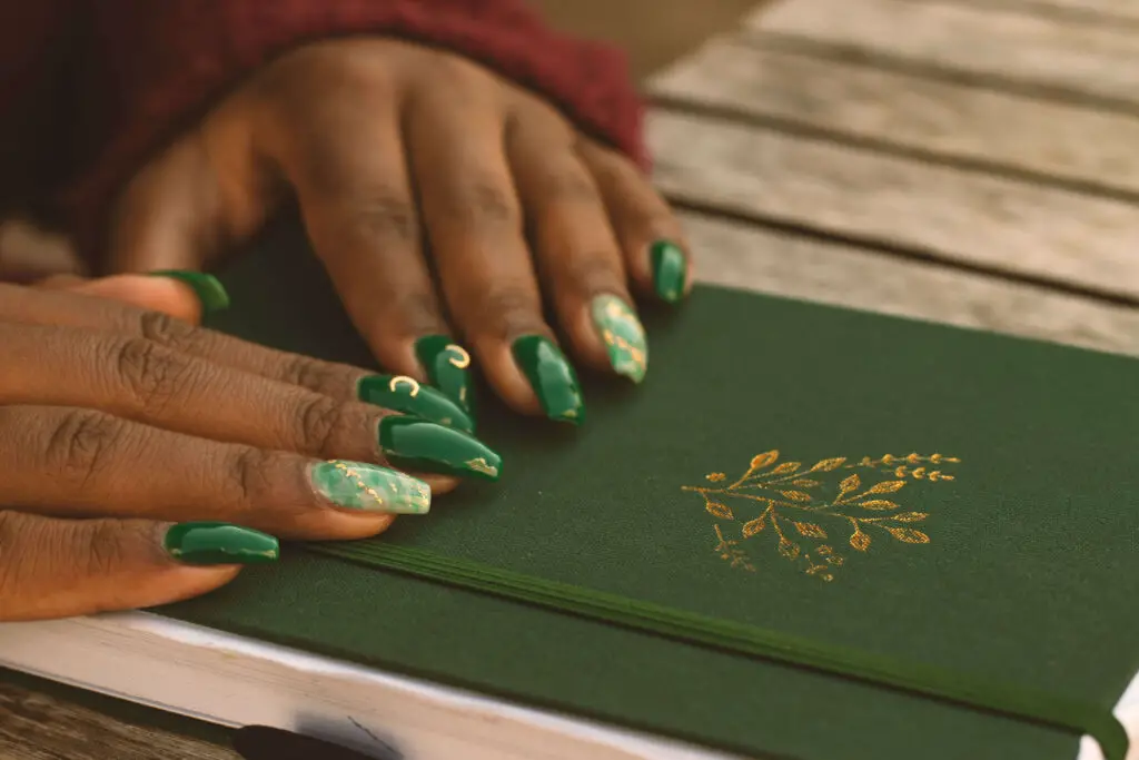 A feminine pair of black hands with elaborately designed green nails settled over a luxurious green-colored journal. Featured image for Bullet Journal for Language Learning article.
